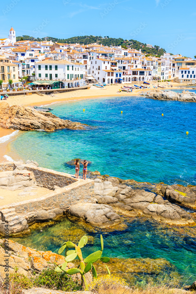 Couple of young woman in swimsuits on amazing beach in Calella de Palafrugell, scenic fishing village with white houses and sandy beach with clear blue water, Costa Brava, Catalonia, Spain