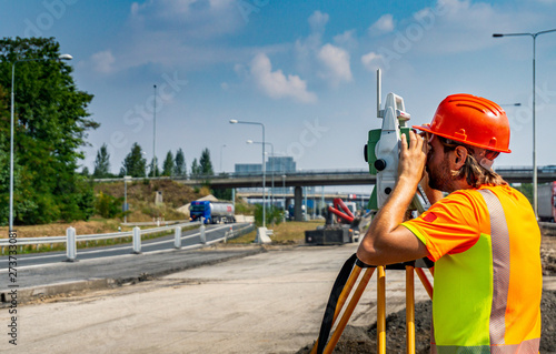 Surveyor engineer or worker with theodolite on construction site of road or highway during the sunny day with blue sky in background