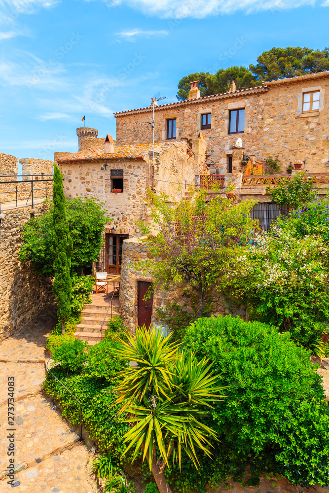Green tropical plants and stone houses in old town of Tossa de Mar, Costa Brava, Spain