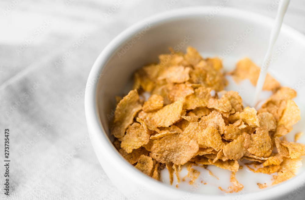 Bowl of breakfast cereals with a swig of milk pouring into it against white rustic wooden background. Concept of healthy breakfast food, clean eating, and dieting. Bowl of breakfast cereals with a swig of milk pouring into it against white rustic wooden background. Concept of healthy breakfast food, clean eating, and dieting.