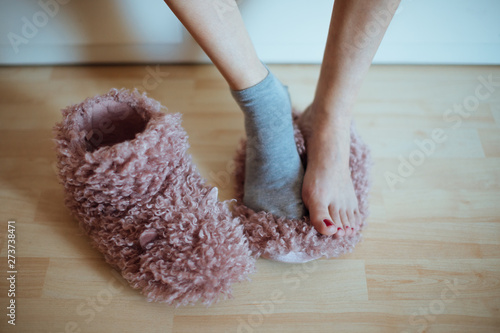Early cold morning wake up! Woman's feet standing on one (of two) home plush slippers - woman wearing only one sock