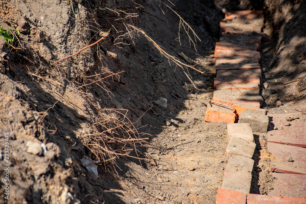 Fototapeta premium Construction ditch with bricks and plant roots