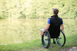 Happy and young disabled or handicapped man sitting on a wheelchair looking at beautiful lake in nature.