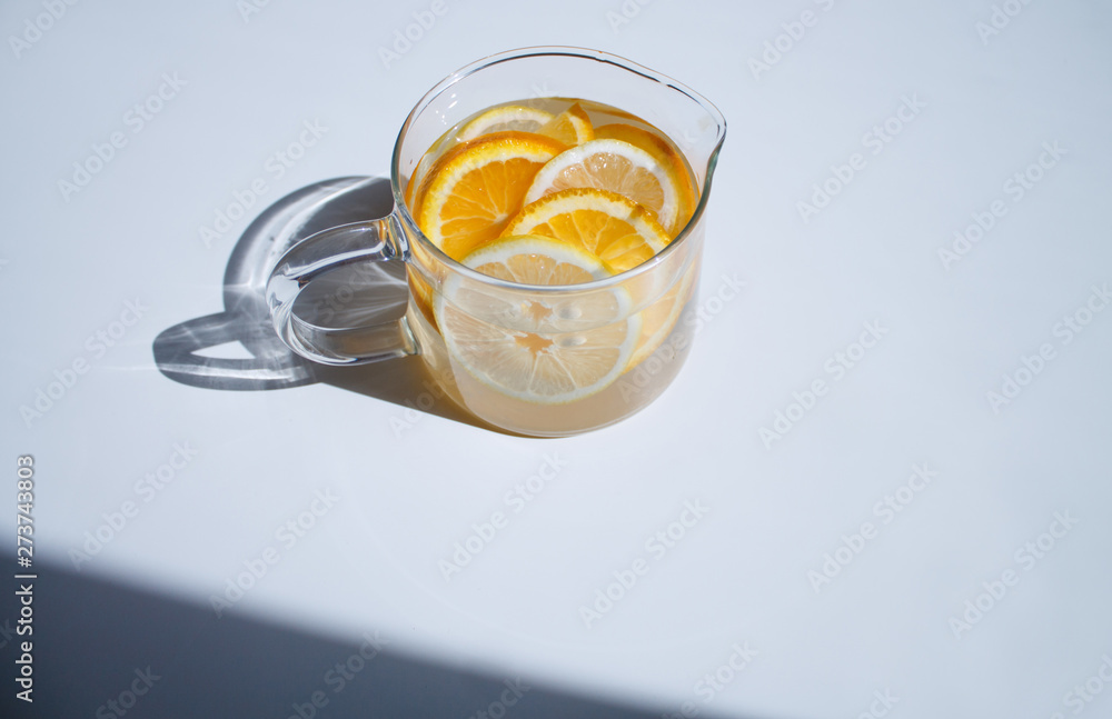 pitcher with lemonade and water sliced oranges and lemon on white table close-up with blurred background