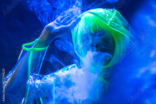 Young pretty unusual Asian woman in plastic transparent raincoat and yellow hair smoking in fluorescent light photo