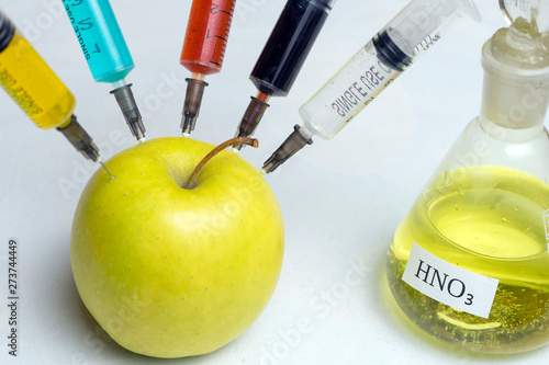 nitrates, pesticides, fungicides and other chemicals are injected into a green apple with a syringe. The concept of GMO and genetically modified organism. Close up.