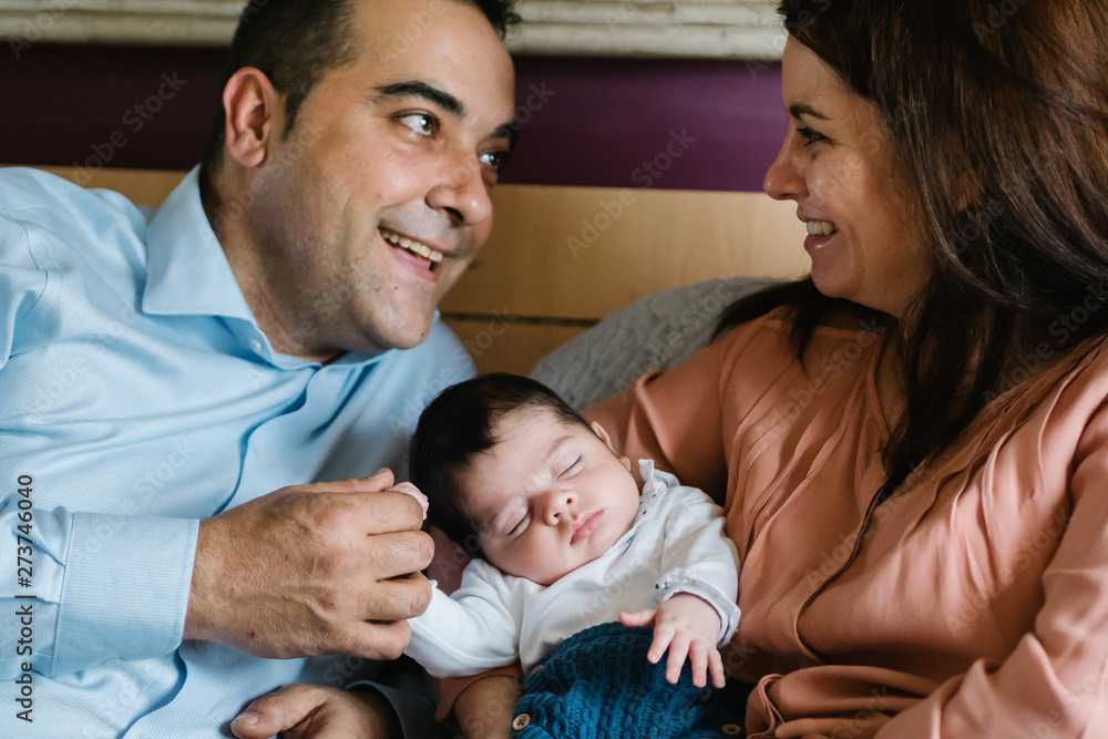 Smiling father holding laughing little daughter lying on bed with mother holding newborn baby Smiling father holding laughing little daughter lying on bed with mother holding newborn baby