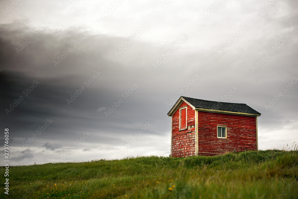 Tiny red building in green grass with dark clouds