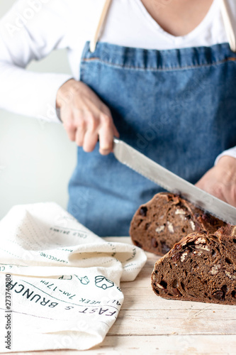 Hands of woman in apron holding long steel knife and cutting rye bread with raisins and nuts photo