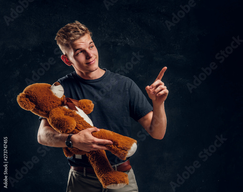Young attractive man is showing something exiting for his friend giand toy bear at dark studio. photo