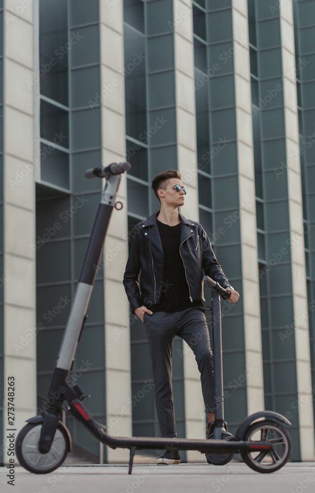 Attractive fashionable man in sunglasses is posing for photographer with two scooters. Attractive fashionable man in sunglasses is posing for photographer with two scooters.