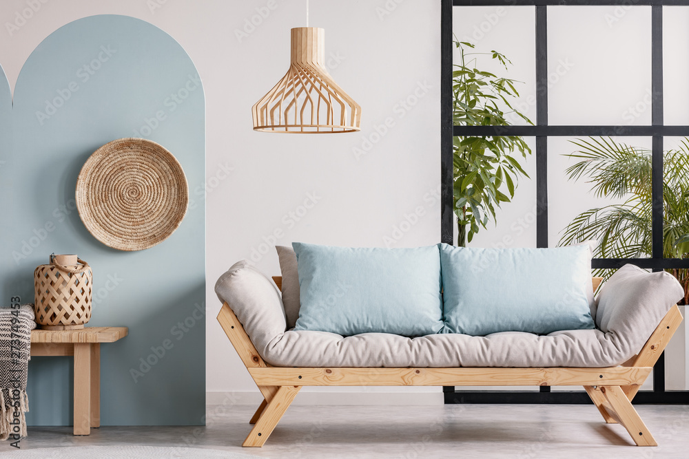 Wicker chandelier above wooden Scandinavian sofa with futon in bright living  room interior foto de Stock | Adobe Stock