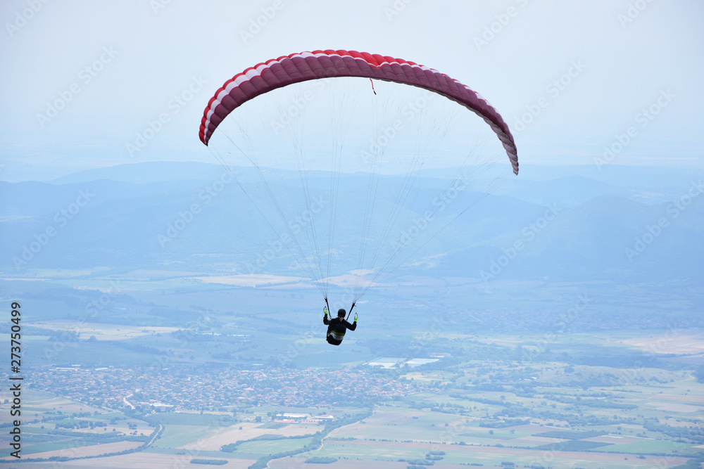 Young woman gliding in the sky above the town of Sopot, Bulgaria. Paragliding jump from the hills of Stara Planina Mountain. Young woman gliding in the sky above the town of Sopot, Bulgaria. Paragliding jump from the hills of Stara Planina Mountain.