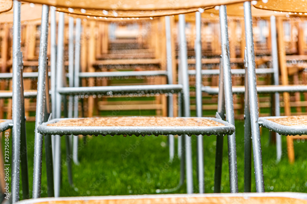 Lot of wooden chairs stand outside in the park in the rain. Empty auditorium, green grass, trees and chairs with waterdrops Lot of wooden chairs stand outside in the park in the rain. Empty auditorium, green grass, trees and chairs with waterdrops