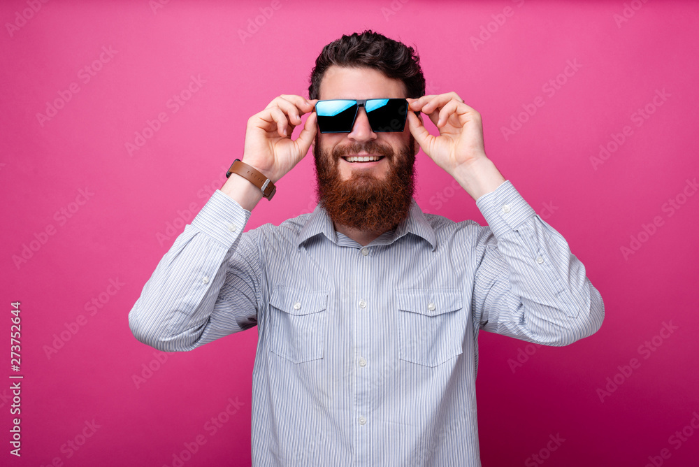 Cool bearded man is wearing sunglasses and white shirt on pink background. Cool bearded man is wearing sunglasses and white shirt on pink background.
