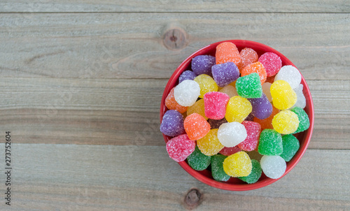 Photography small red bowl filled with brightly colored candy gumdrops on a wood background