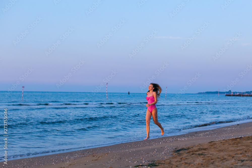 girl in a pink swimsuit run on a sand beach near the sea.
