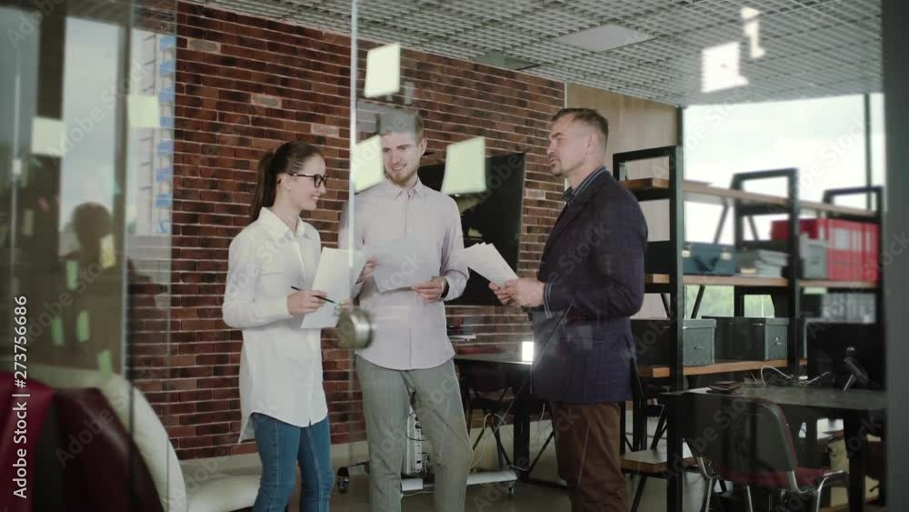 group of young businesspeople standing together in a modern office watching their manager draw a graph on a glass wall group of young businesspeople standing together in a modern office watching their manager draw a graph on a glass wall