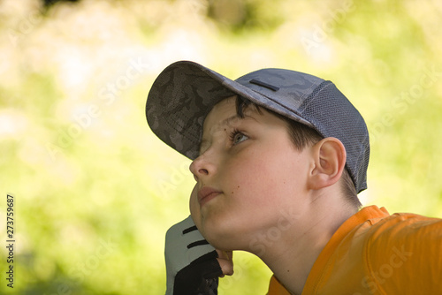 The boy is resting on a natural background, propping his cheek with his hand