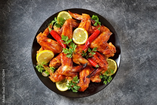 Delicious grilled chicken wings with lemon juice and chili pepper on black concrete background. Top view. 