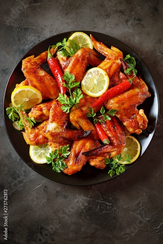Delicious grilled chicken wings with lemon juice and chili pepper on black concrete background. Top view. 
