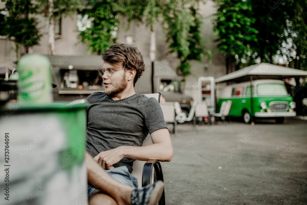 young hipster male with beard and glasses sits on street cafe on retro car background
