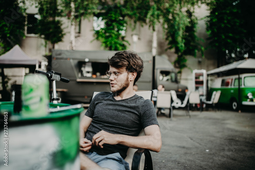 young hipster male with beard and glasses sits on street cafe on retro car background