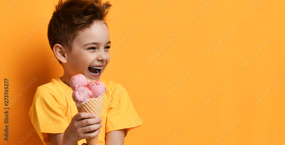 Baby boy kid hold strawberry pink ice-cream in waffle cone happy laughing looking at the corner on yellow Baby boy kid hold strawberry pink ice-cream in waffle cone happy laughing looking at the corner on yellow