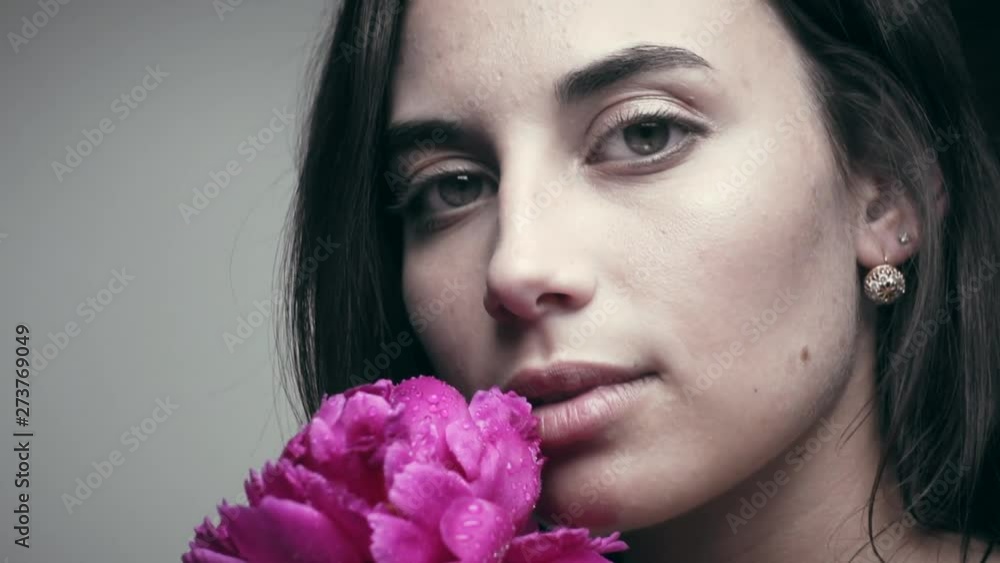 Young woman with pionie flower in studio on gray