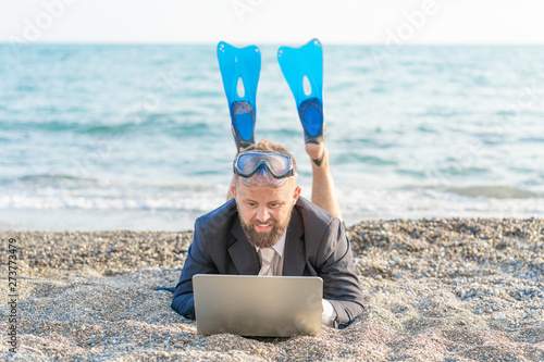 Successful businessman wearing snorkeling tools is working on the beach with laptop