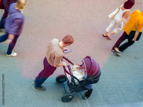 An adult male husband stands next to the stroller with a baby.