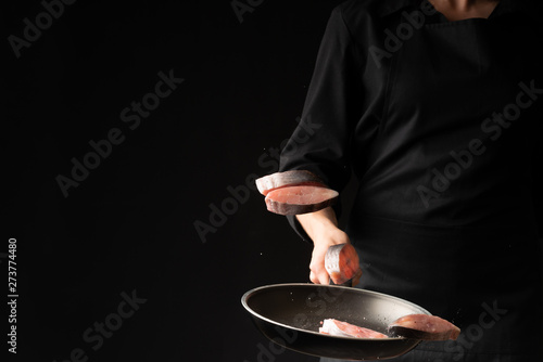 Chef cook fry fish in a griddle on a black background. horizontal photo. sea food. healthy food. oriental cuisine