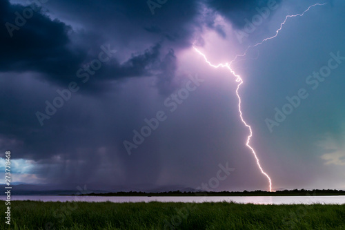 Heavy thundercloud with lightning striking the earth on the opposite shore of the lake. Lightning storm.