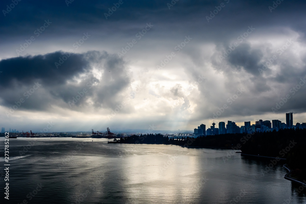Sun rays in dark clouds over city and water in Vancouver, BC, Canada.