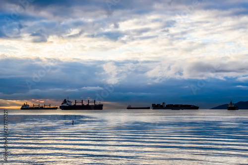 Cargo ships at cloudy dusk in bay.