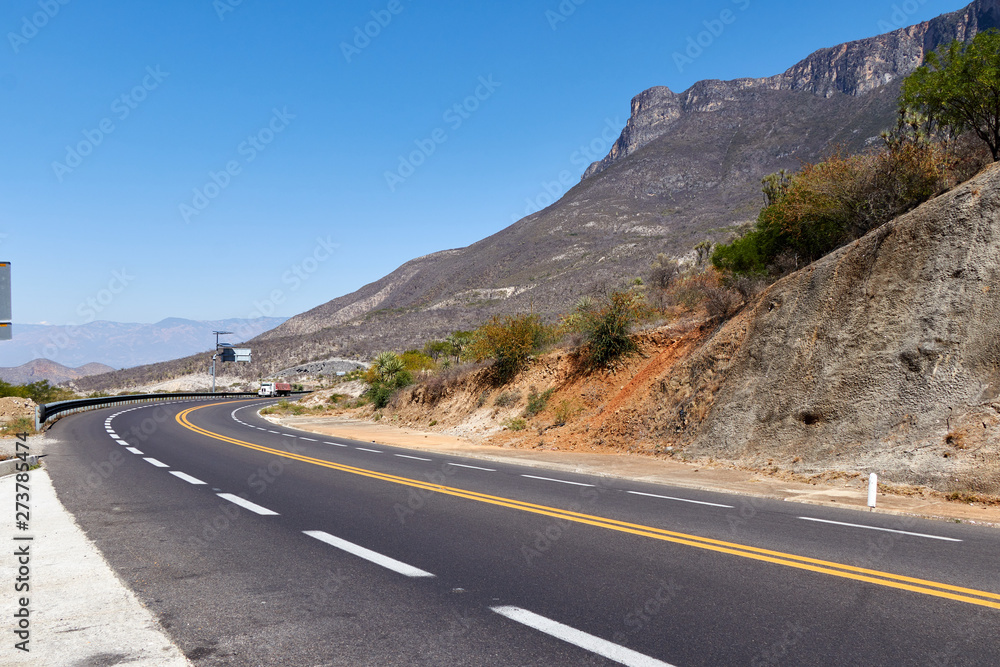 road curve between rocky and arid mountains at noon and clear sky