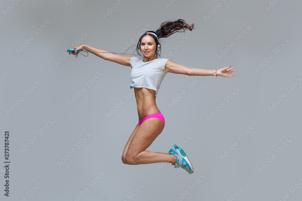 Energy young sexy brunette lady woman listening music in headphones isolated on gray background. Charming caucasian girl in earphones enjoying music and dancing. Jumping up, flying.