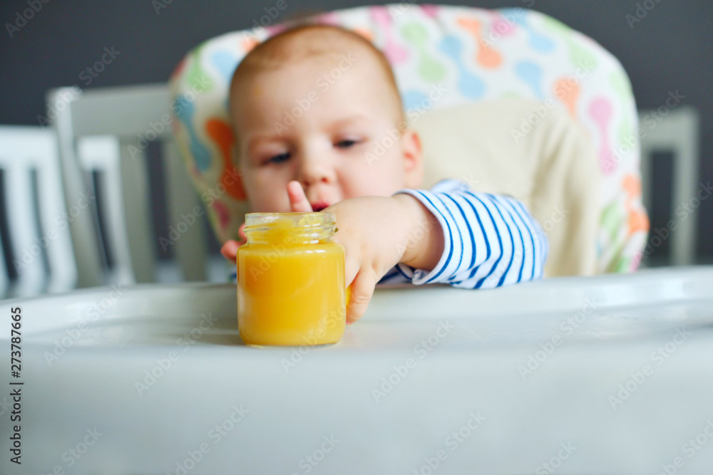 Happy boy 7-8 months eats Apple/pear puree with spoon in kitchen at home. Baby food, solid food concept. Happy boy 7-8 months eats Apple/pear puree with spoon in kitchen at home. Baby food, solid food concept.