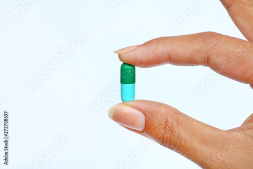 Finger holds pill on white background