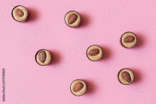 Round chocolates with pistachio cream and salted almonds on pink background. Flat lay