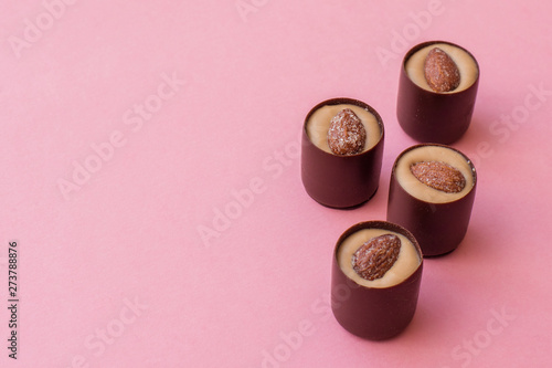 Round chocolates with pistachio cream and salted almonds on pink background. Copy space