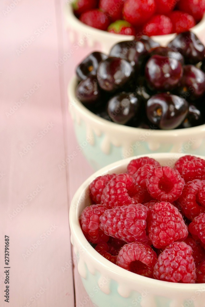 Raspberries, strawberries, sweet cherry berries in round cups . Summer berries mix on pink pastel wooden background. Berry season. Raspberries, strawberries, sweet cherry berries in round cups . Summer berries mix on pink pastel wooden background. Berry season.