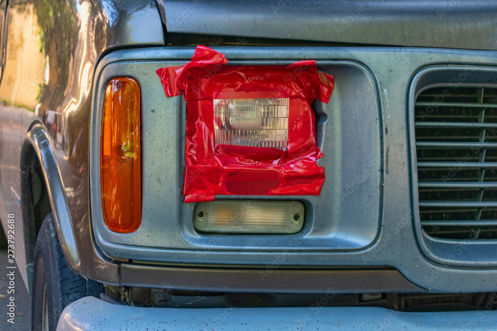 Broken headlight fixed by red duct tape. Car accident, insurance concept with adhesive tape on
