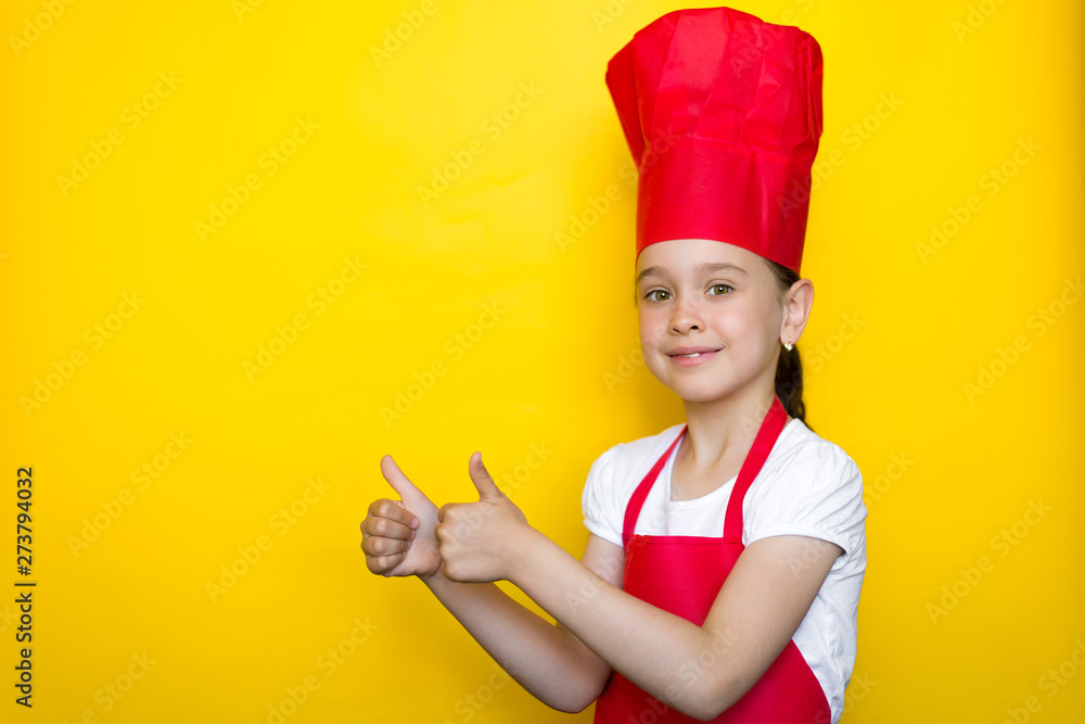 smiling girl in a red chef's suit and showing thumb's up gesture on a yellow background with copy space smiling girl in a red chef's suit and showing thumb's up gesture on a yellow background with copy space