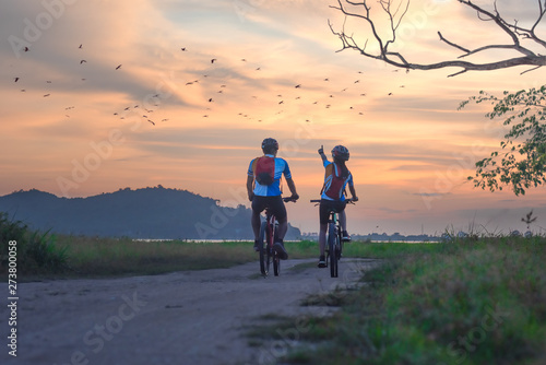 couple lover biker cyclist riding enjoyment to the field of meadow lake at sunset, adventure bicycle wild and journey activity.