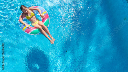 Acrive girl in swimming pool aerial top view from above, kid swims on inflatable ring donut , child has fun in blue water on family vacation resort