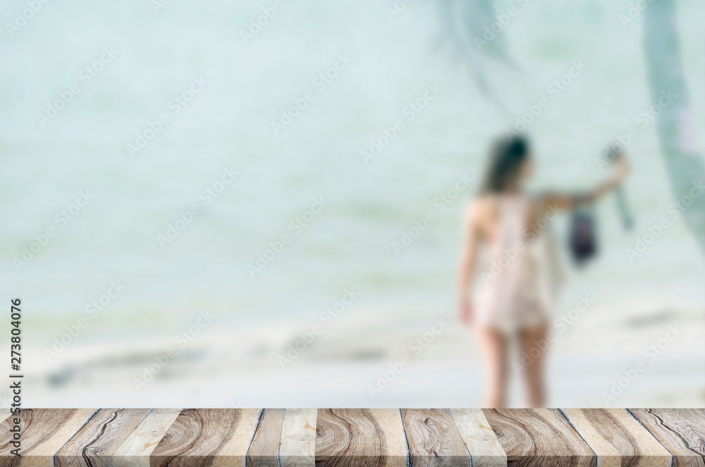 Top wooden table with blurred summer beach and woman taking photo background.