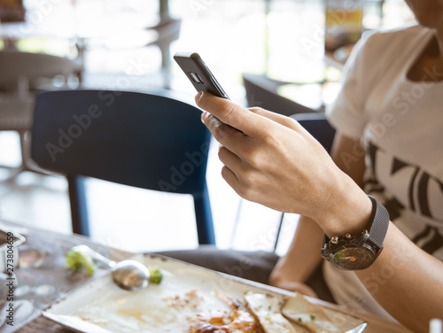 Close up of man hand using or looking at his smartphone and having lunch in the restaurant.