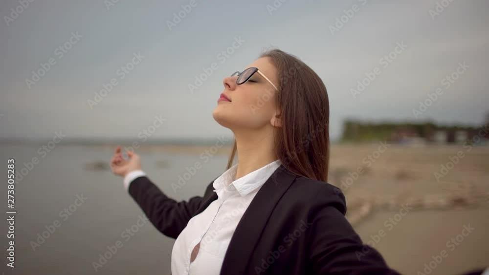 Calm businesswoman relaxing ang meditating at beach nature. Young yoga arms raised woman girl female wearing glasses inhaling, exhaling fresh air, enjoying breathing outdoors, calming, no stress relax