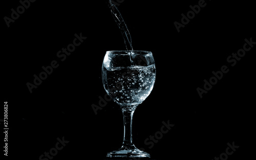 Pour water into glass on black background.